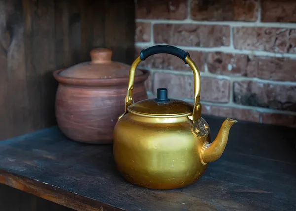 Ancienne bouilloire en or sur une vieille étagère en bois. Théières classiques à utiliser pour boire du thé ou du café. Pot d'argile en arrière-plan — Photo