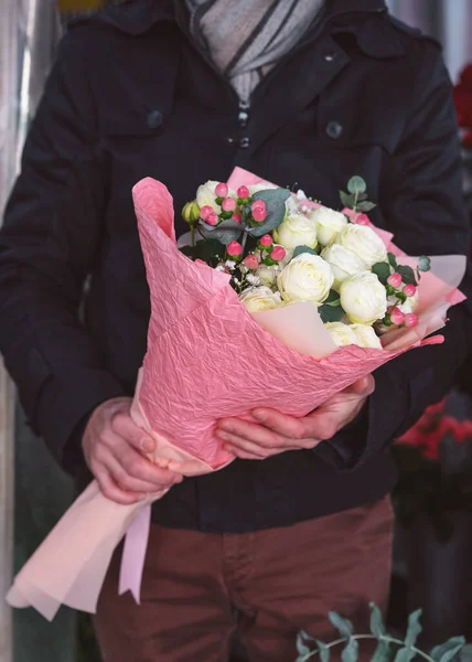 Jeune homme tenant un beau bouquet de fleurs en gros plan. Homme vêtu d'une veste chaude et écharpe. Des gens méconnaissables. Plan vertical — Photo