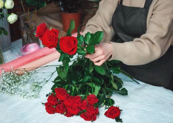 Fleuriste femme créant un bouquet de roses rouges fraîches. Image recadrée d'une fleuriste qui arrange des fleurs de roses à l'aide d'outils. Concept de travail avec des fleurs, affaires florales. Concentration sélective. — Photo