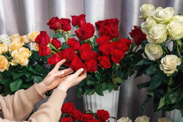 Designer floral debout à côté de la table avec des vases à fleurs. Gros plan mains de fleuriste touchant fleurs fraîches. Rosse rouge vif, orange et blanche. Concept de fleurisme. Le travail dans un magasin de fleurs — Photo