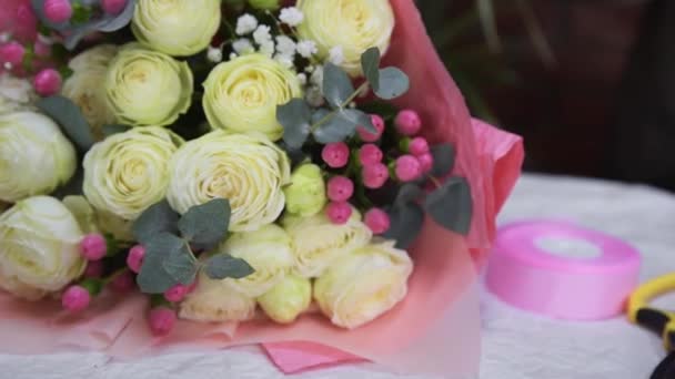 Close-up mooi vers boeket van witte rozen en decoratieve bloemen verpakt in roze ambachtelijke papier — Stockvideo