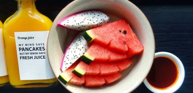 Taze karpuz ve tabakta ejderha meyvesi ve siyah ahşap masada bir şişe portakal suyu. Ahşap arka planda taze meyvenin düz uzanması. Sağlıklı yemek ve diyet.