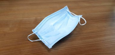 Kahverengi ahşap arka planda kullanılmış yüz, doktor ya da tıbbi maske. İnsanların tozu, korona virüslerini (COVID-19) ve salgını önlemek için koruyucu maske takmalarına yönelik bir kampanya. Kendinize iyi bakın.