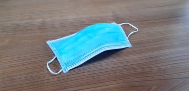 Kahverengi ahşap arka planda yüz, doktor ya da tıbbi maske. İnsanların tozu, korona virüslerini (COVID-19) ve salgını önlemek için koruyucu maske takmalarına yönelik bir kampanya. Kendinize iyi bakın.