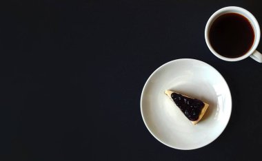 Beyaz tabak ya da tabakta dilimlenmiş yaban mersinli cheesecake ve fotokopi alanı ile kaplanmış siyah kahve. Atıştırmalık ya da bir parça tatlı yemek ve bir fincan çay ya da masada içmek..  