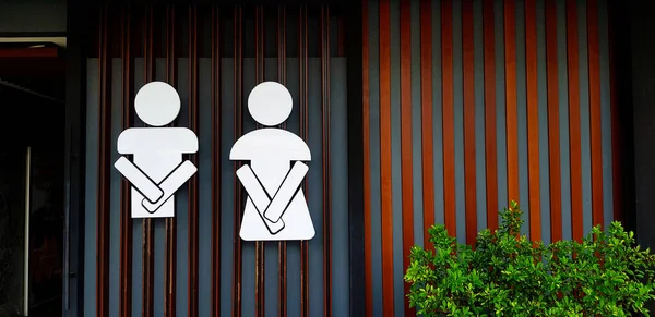 灰色或灰色墙壁背景上带有复制空间的男女公共厕所标志或符号 房间前面有一棵树的卫生间或厕所入口 免版税图库照片