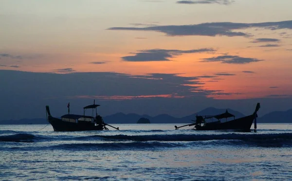 Two silhouette of longtail boat on sea and wave with orange sky and cloud background at Krabi, Thailand. Landscape of ocean at sunset time.