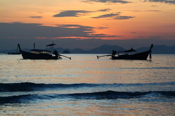 タイのクラビでは オレンジ色の空と雲の背景を持つ海と波の上に長い尾のボートの2つのシルエット 日没時の海の風景 — ストック写真