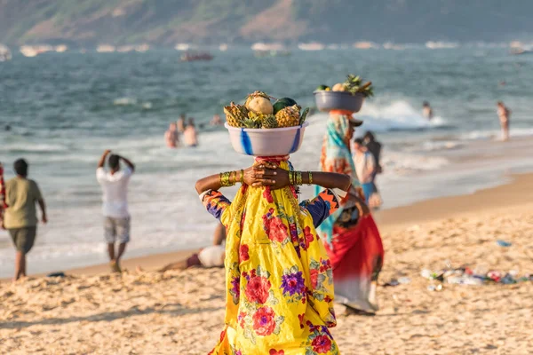 Kıyı şeridinde turistlere, CALANGUTE 'a, GOA' ya, INDIA 'ya sattığı için kafasında taze meyve taşıyan pembe mavi sari elbiseli tanımlanamayan Hintli kadın.