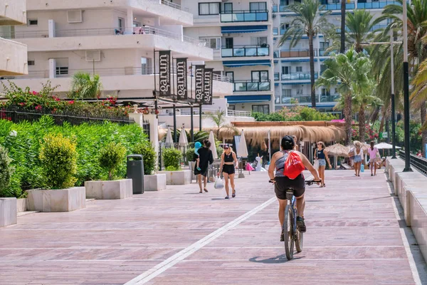 Marbella 'da deniz kıyısında yaya caddesinde dağ bisikleti süren genç kadınların arka manzarası. Marbella, Malaga / İspanya - 21 Temmuz 2022