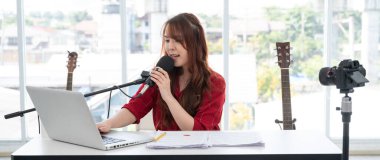Asyalı kadın evinde mikrofon ve bilgisayarla canlı yayın veya video blogu hakkında konuşuyor