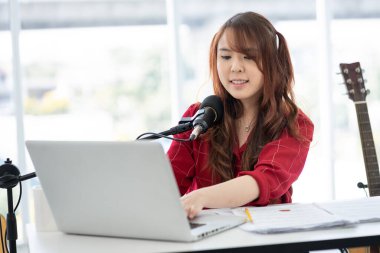 Asyalı kadın evinde mikrofon ve bilgisayarla canlı yayın veya video blogu hakkında konuşuyor