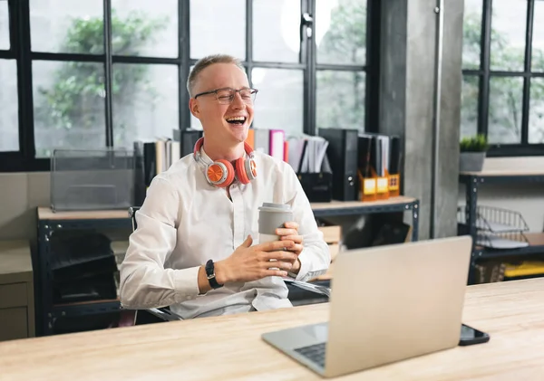 Mutlu iş adamı ofiste dizüstü bilgisayarla güler.