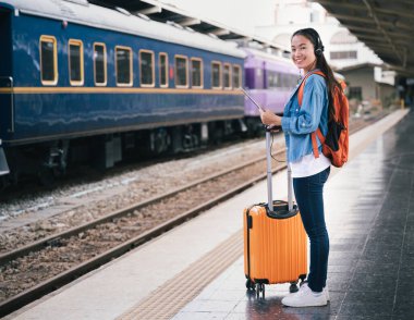 Tren istasyonunda çantalı ve turuncu çantalı gezgin kadını kopyala.