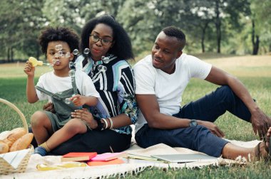 Mutlu piknikler, rahatlayın. Bahçede baloncuk patlatan oğlu olan siyahi aile.