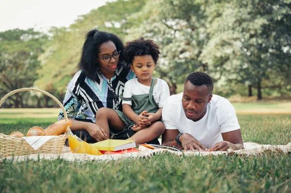 Mutlu piknikler, rahatlayın. Siyahlar, aileler ve oğullar bahçede. Sepette ekmek var.