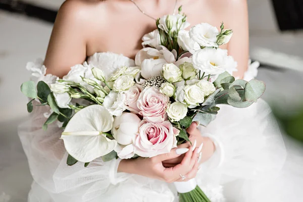 beautiful wedding bouquet in the hands of a charming bride.  Close-up of a brides bouquet in white-peach shades. The bride in a  white dress holds a bouquet in her hands. White sand. Close-up bunch of florets. Bridal accessories