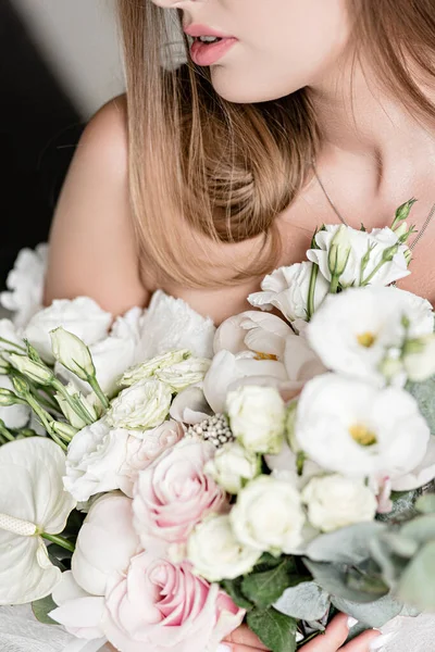 beautiful wedding bouquet in the hands of a charming bride.  Close-up of a brides bouquet in white-peach shades. The bride in a  white dress holds a bouquet in her hands. White sand. Close-up bunch of florets. Bridal accessories.