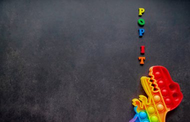 Oyuncak dinozor gökkuşağı renginde siyah arka planda çok renkli harfler ve harfler var. Boşluğu kopyala.