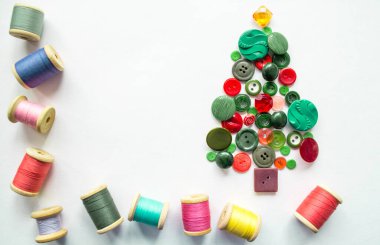 Düğmelerden yapılmış bir Noel ağacı, yeşil, kırmızı renk. Ahşap makaralı çok renkli iplikler. Beyaz arkaplan, kopyalama alanı. Yaratıcı Noel kavramı.