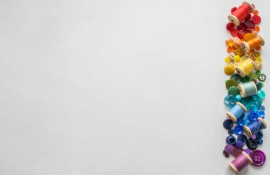 Renkli ipliklerle bir sürü düğme ve makara, gökkuşağının renginde beyaz bir arka planda serili. Boşluğu kopyala.