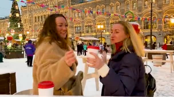赤の広場にモスクワのクリスマスフェア 2人の陽気な若い女性と段ボールカップホットドリンクダンスと笑い — ストック動画