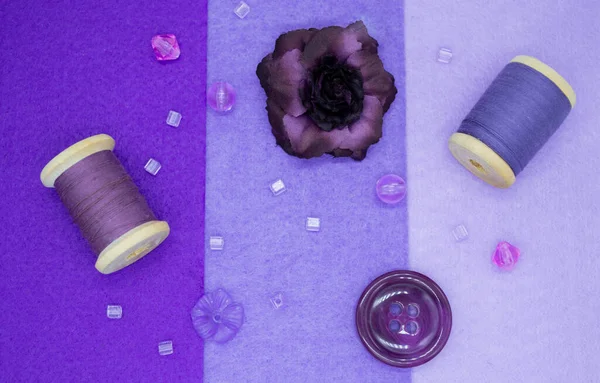 Purple sewing items: felt in three shades of lilac, wooden spools with thread, beads, buttons, and a purple rose.