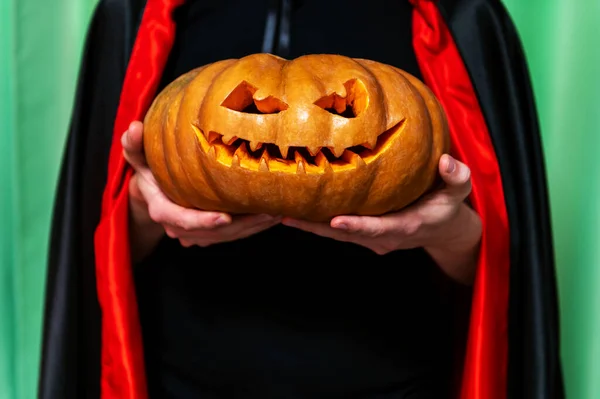Un hombre con una capa de Drácula negra y con una calabaza para Halloween en sus manos, — Foto de Stock