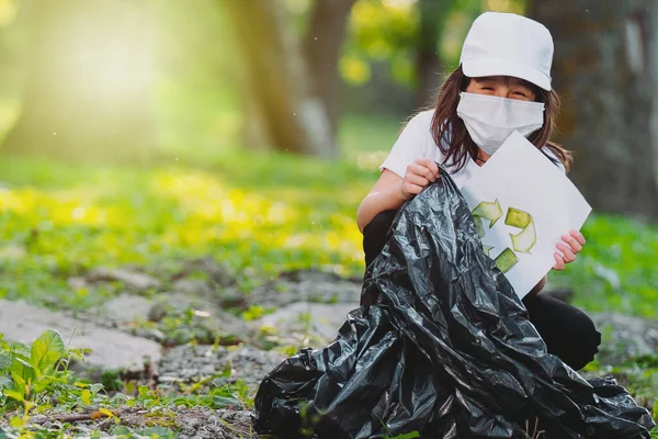 近照：一个戴着医疗面具的漂亮的笑容可亲的女孩，把写有回收标志的废纸放进垃圾袋里淹死了，抄写文字. — 图库照片