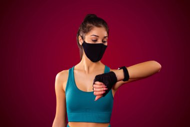 Tekstil maskeli çekici genç bir kadın spor kıyafetleri giyiyor ve spor kıyafetleri giyiyor. Salgın hastalıklar üzerinde antrenman yapmak için akıllı gözlük kullanıyor..