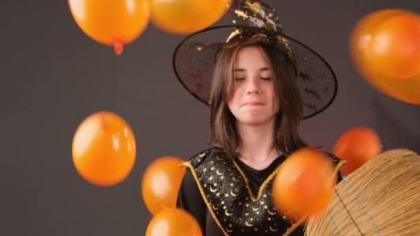 Close up video of a magician girl holding the broom in her hands and someone throws orange balloons at her, she is laughing. — Stock Video
