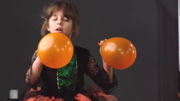 Умная красивая девушка в Хэллоуинском платье с двумя оранжевыми шариками в руках, направляя воздушные шары к лицу и выпуская воздух. — стоковое видео