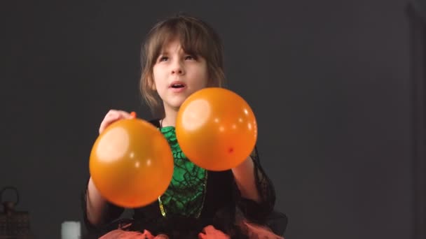 Klein mooi meisje in een mooie jurk opblazen ballonnen oranje kleur op haar beurt met haar mond in haar handen voor de Halloween feest. — Stockvideo