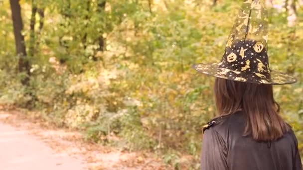 할로윈 의상을 입고 모자를 쓰고 홀로 가을 숲을 걷고 있는 소녀, 마술같은 개념. — 비디오