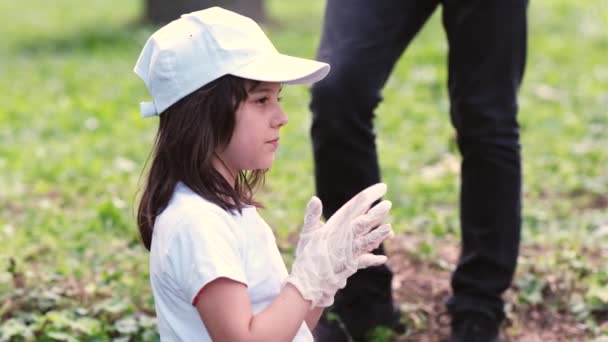 Guarda il video laterale di una bella ragazza in berretto bianco e t-shirt raddrizza guanti e sbadigli mentre fa volontariato per raccogliere la spazzatura. — Video Stock