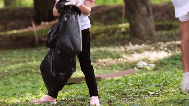 Twee vrijwilligers meisje en een man met beschermende handschoenen het oprapen van het afval buiten en zet het in de grote zwarte zak. — Stockvideo