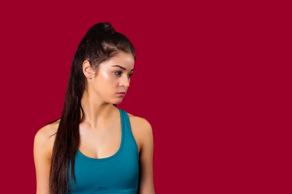 Профиль фото спортивной молодой девушки в синем топе и длинный хвост брюнетки устал после тренировки, позирует на красном фоне в студии. — стоковое фото