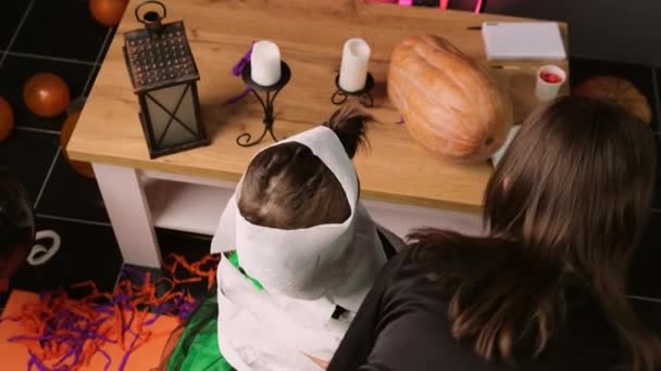 La niña juega el papel de una momia y todo el cuerpo de la pequeña hermana mayor está envolviendo en papel higiénico para la fiesta de Halloween. — Vídeo de stock