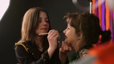 Küçük kızın üzerine çizim yapan genç kız, siyah boya ve fırçayla Cadılar Bayramı maskesi takıyor. Partiye hazırlanıyorlar. Yüksek kalite 4k görüntü