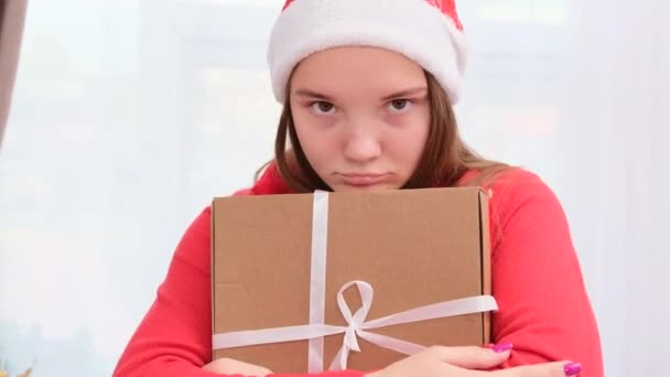 Κοντινό πλάνο βίντεο ενός κοριτσιού σε ένα καπέλο Σάντα με λυπημένη έκφραση προσώπου κρατώντας το δώρο και δεν θέλει να σας δώσει κανέναν. — Αρχείο Βίντεο