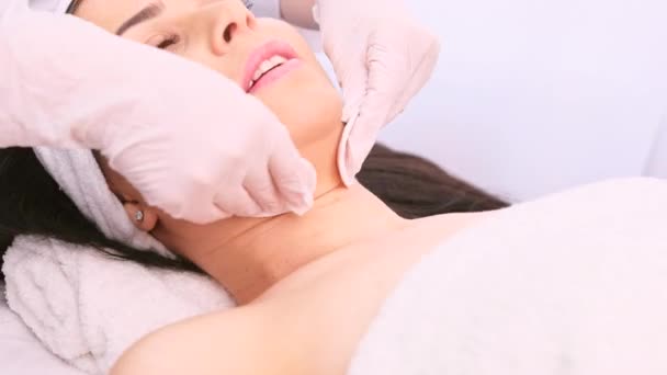 Красива молода жінка, яка отримує омолоджуючу процедуру на обличчі в клініці косметолога, носить медичні рукавички та використовує бавовняні подушечки . — стокове відео