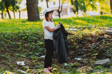 Dışarıda gönüllü çalışan, eldivenli, elinde çöp torbası tutan bir kızın yan görüntüsü. Çevre kavramı..