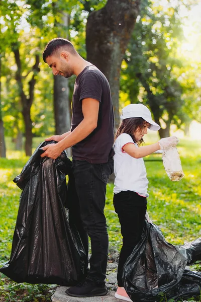 Full längd foto av en man och en flicka som står tillbaka till baksidan utomhus håller soppåsar och samla skräp. — Stockfoto
