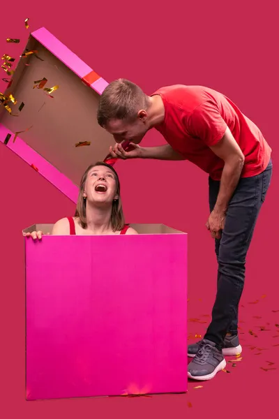 Büyük pembe bir hediye kutusunu açan bir erkek arkadaşın ilginç bir fotoğrafı ve içinde gülen yüz ifadesiyle kız arkadaşını görüyor.. — Stok fotoğraf