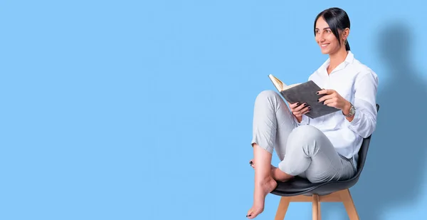 Foto de larga duración de una atractiva dama de negocios feliz vestida de blanco sentada en una silla con las piernas cruzadas sosteniendo el diario de negocios, espacio para copiar. — Foto de Stock