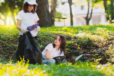 İki genç kızın fotoğrafını kapatın çöpten doğayı temizlemeye katılın, plastik çöpleri torbaya doldurun..