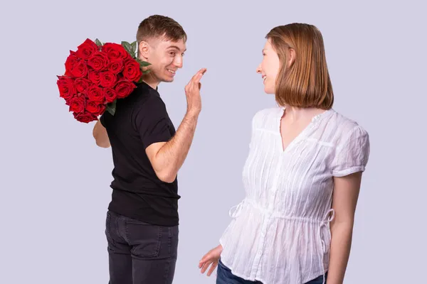 Dostawca patrząc na kobietę z uśmiechem trzymającą wielki bukiet czerwonych róż podniósł rękę, kobieta blondynka odwróciła głowę w kierunku kuriera. — Zdjęcie stockowe