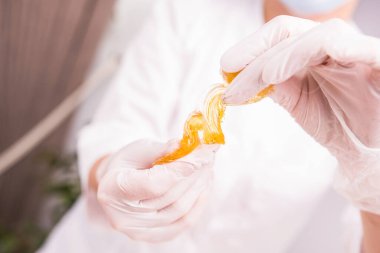 Seçici odaklanma. Güzellik salonunda balmumu karıştırıcı macun tutan koruyucu eldivenli bir kozmetik uzmanı kadının fotoğrafını çek..