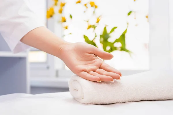 Close up photo of a cropped cosmetologist woman hand, female palm up on a folded white towel in a beauty salon, health and clean concept. Yellow natural flowers. Ready for massage — Stock Photo, Image