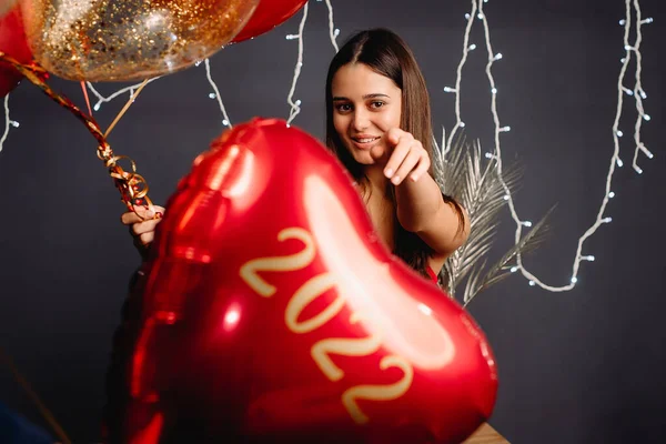 Güzel genç mutlu kız kalp şeklinde balonlarla poz veriyor kırmızı renk ve aydınlatma gri arka planda, yeni yıl konsepti. — Stok fotoğraf